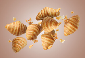 Delicious croissants and crumbs in air on pale brown background. Puff pastry