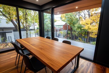 Modern dining room interior with wooden table chairs and large windows overlooking autumn trees and houses contemporary design and natural light