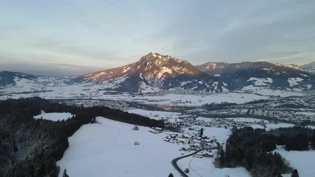 Snow-covered Gunzesrieder Tobel and Gunzesrieder Ach seen from above, with dense frosty forests, frozen reservoir, and white-coated alpine slopes stretching across the horizon.