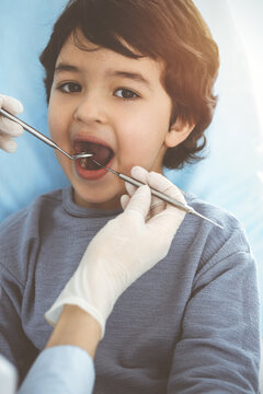 Cute arab boy sitting at dental chair with open mouth during oral checking up with doctor. Visiting sunny dentist office