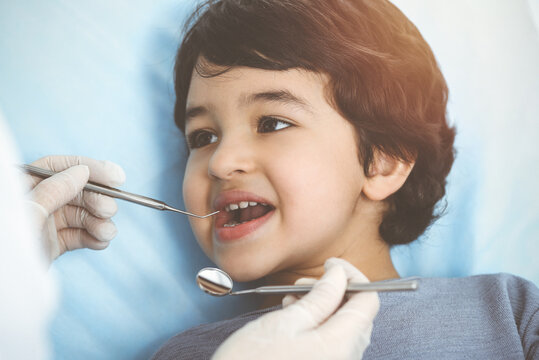Cute arab boy sitting at dental chair with open mouth during oral checking up with doctor. Visiting sunny dentist office