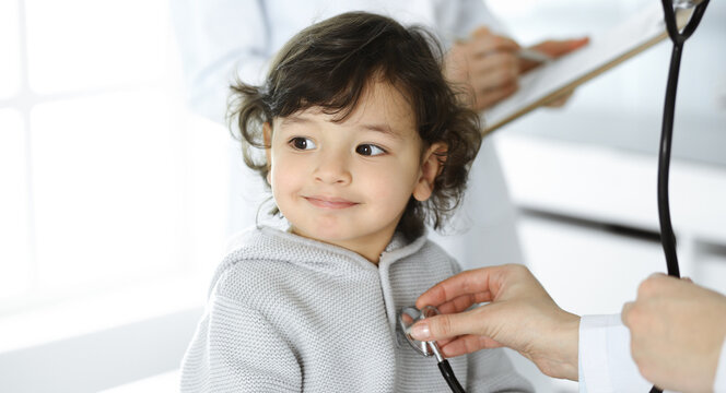 Woman-doctor examining a child patient by stethoscope. Cute arab toddler at physician appointment. Medicine concept