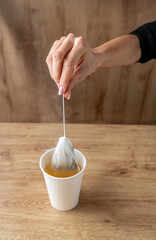female hand dips a tea strainer into a glass with hot water preparing a warm and relaxing drink on a light wood background, conceptual and vertical photo theme pause , break relaxation and home life