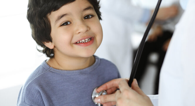 Doctor-woman examining a child patient by stethoscope. Cute arab boy and his brother at physician appointment. Medicine concept