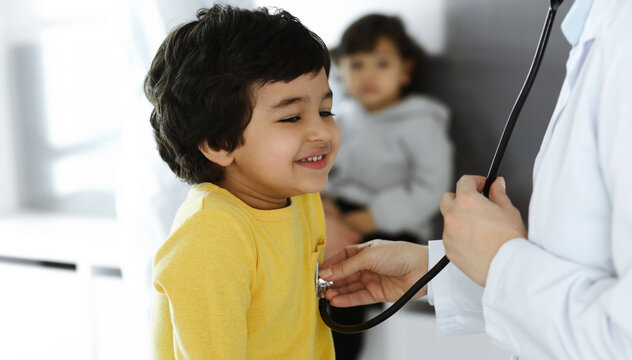 Woman-doctor examining a child patient by stethoscope. Cute arab boy at physician appointment. Medicine help concept
