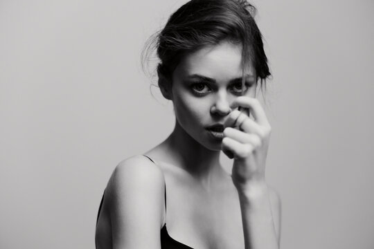 Thoughtful young woman in a minimalist black and white portrait, gently touching her face with an introspective expression. Beauty and emotion concept.