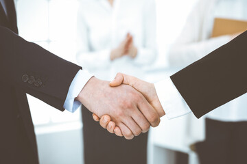 Businessman and woman shaking hands with colleagues at the background. Handshake at meeting in office. Concept of success in business