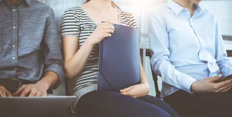 Group of casual dressed business people sitting in a line while waiting for a job interview in sunny office