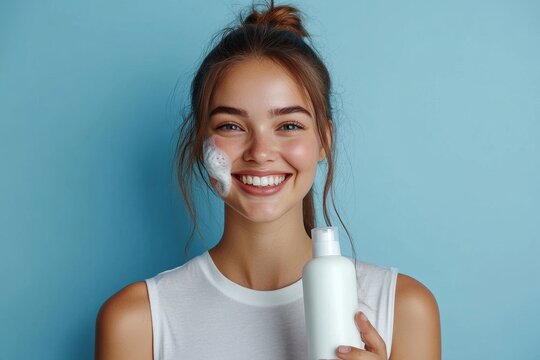 Cheerful laughing woman applying cleansing foam for washing face, blue background. Skincare and beauty routine concept
