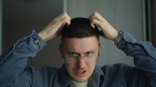 A man with glasses scratches his head with his hands.
A person experiences scabies on his head.
A guy has scalp problems.
A young man's head itches.
Scratching, head, dandruff