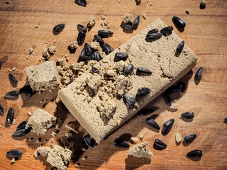 Block of halva with pieces and sunflower seeds on wood, top view, studio shot