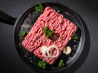 Minced meat with pepper, salt, onion and parsley leaves in a pan, top view, studio shot