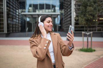 Fototapeta premium Businesswoman listening to music on headphones and holding smartphone in urban setting