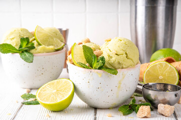 Summer refreshing cold dessert, tasty aromatic mojito or key lime pie ice cream, homemade sorbet with mojito cocktail flavor in ceramic bowl, with fresh lime, mint, waffle cones on wooden background