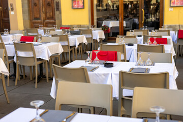 Restaurant tables waiting for customers at an outdoor terrace. Cozy outdoor cafe. Table served for a lunch or dinner, with vine glasses