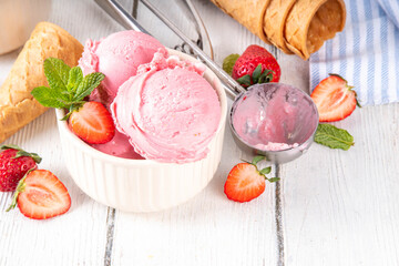 Summer refreshing cold dessert, tasty and aromatic strawberry ice cream, homemade berry sorbet in ceramic bowl, with fresh strawberries, ice cream waffle cones on white wooden background