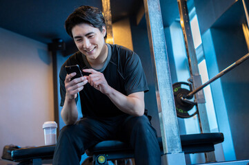 トレーニングジムでスマホを使ってメニュー管理する日本人男性