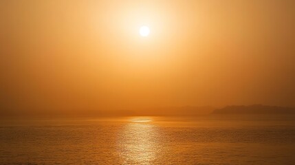 Fototapeta premium Hazy summer horizon showing the sun setting over a calm sea during a heatwave