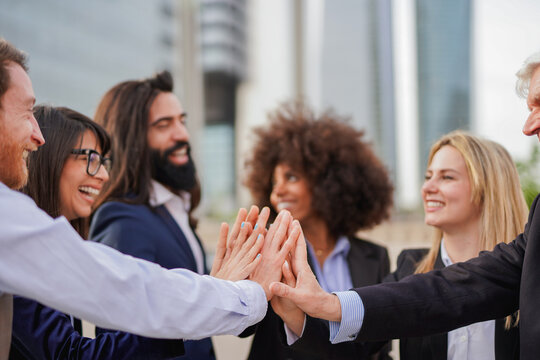 Group of multi generational business people stacking hands outside of financial building - Confident multiracial entrepreneurs in the city with cityscraper in background - Focus on senior man hand