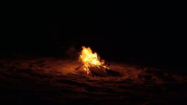 A burning campfire in winter, at night. A bright flame in total darkness. Sparks fly, the bonfire gives warmth and light.