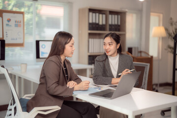 Two asian businesswomen are discussing marketing strategy using laptop and taking notes in modern office, businesswomen discussing new project planning