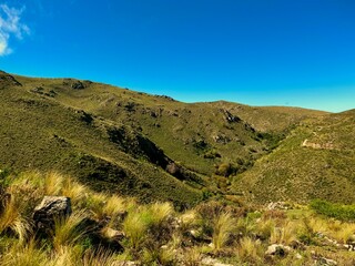 Green hills covered with grasslands, a rocky trail, blue sky with clouds and a valley in the distance