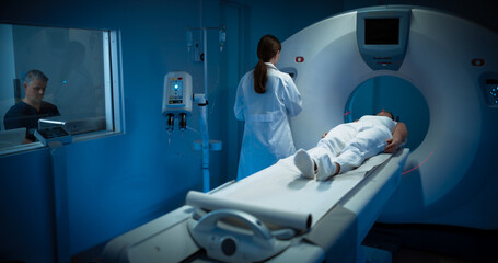 High-Tech Modern Medical Equipment: In Medical Laboratory Male Radiologist and Female Doctor Control and Monitor MRI or CT Scan with Female Patient Undergoing Health Procedure
