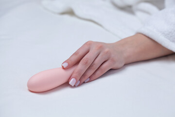 The girl is lying in a white bed. A woman holds a pink dildo in her hand. Toys for adults.