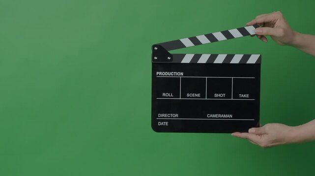 A classic black and white film clapperboard or movie slate being held in front of a green screen. Essential filmmaking tool is used to mark scenes and synchronize audio and video in film production.
