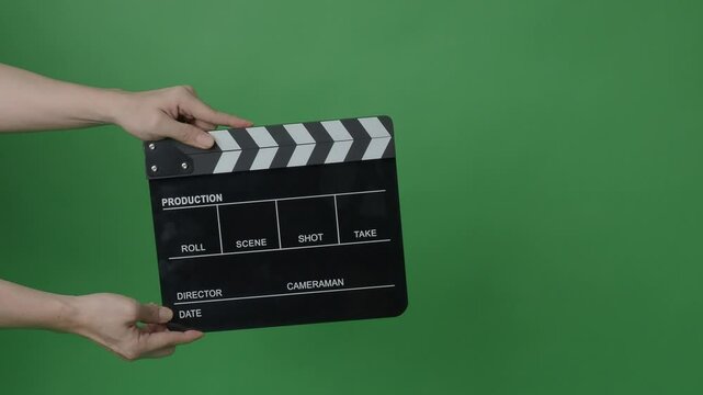 A classic black and white film clapperboard or movie slate being held in front of a green screen. Essential filmmaking tool is used to mark scenes and synchronize audio and video in film production.