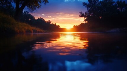 Obraz premium A tranquil river reflects the vibrant colors of a sunset. The scene captures the beauty of nature, with trees lining the bank and a serene atmosphere perfect for relaxation.