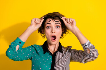 Photo of impressed astonished woman wear stylish clothes hold glasses isolated on yellow color...
