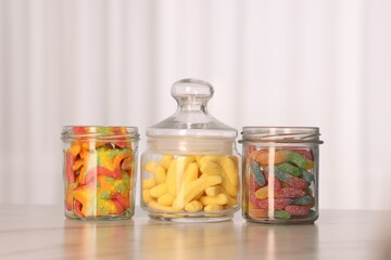 Tasty gummy candies in glass jars on white marble table
