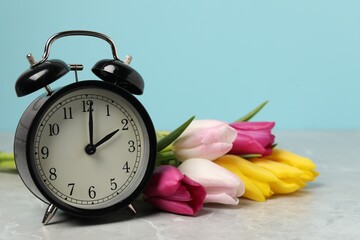 Spring time. Alarm clock and beautiful tulips on grey marble table against light blue background