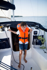 Młody chłopiec ubrany w pomarańczową kamizelkę asekuracyjną śmieje się i bawi na jachcie z rodzicami, bezpieczne wakacje na wodzie i jachcie © Katarzyna Krociel