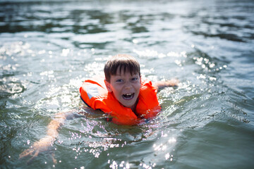 Młody chłopiec ubrany w pomarańczową kamizelkę asekuracyjną śmieje się i bawi na jachcie z rodzicami, bezpieczne wakacje na wodzie i jachcie © Katarzyna Krociel