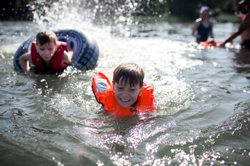 Młody chłopiec ubrany w pomarańczową kamizelkę asekuracyjną śmieje się i bawi na jachcie z rodzicami, bezpieczne wakacje na wodzie i jachcie © Katarzyna Krociel