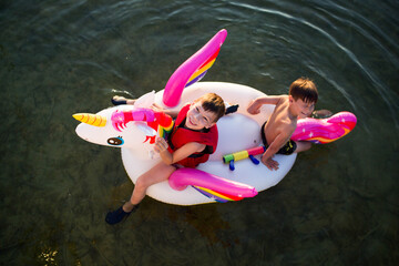 Dzieci pływają na dmuchanym jednorożcu, bawią się i pluskają w wodzie, słońce pięknie świeci © Katarzyna Krociel