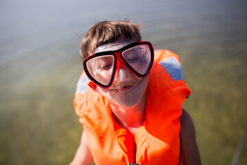 Młody chłopiec ubrany w pomarańczową kamizelkę asekuracyjną śmieje się i bawi na jachcie z rodzicami, bezpieczne wakacje na wodzie i jachcie © Katarzyna Krociel