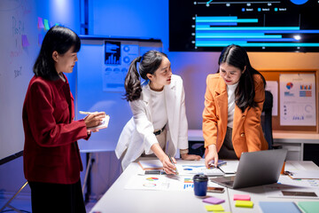 Three women are sitting at a table with a laptop and papers