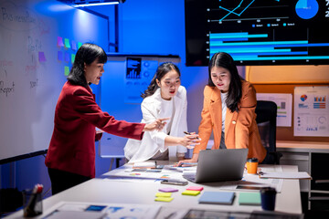 Three women are sitting at a table with a laptop and a whiteboard