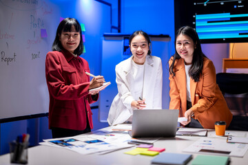 Fototapeta premium Three women are smiling and standing around a table with a laptop