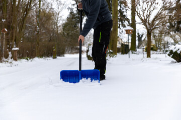 Schnee mit einem blauen Schneeschieber im Winter schieben