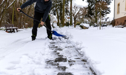 Schnee mit einem blauen Schneeschieber im Winter schieben