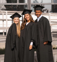 Happy graduated students smiling and wearing black graduation gowns