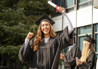 Excited student female celebrating graduation with arms raised and diploma in hand