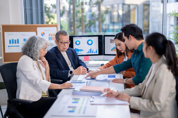 A group of people are sitting around a table with papers and graphs