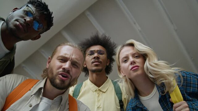 Bottom view four friends multiracial diversity students African American male men guys Caucasian woman girl female in university looking at camera grimacing awful terrible smelly bad ugly disgust
