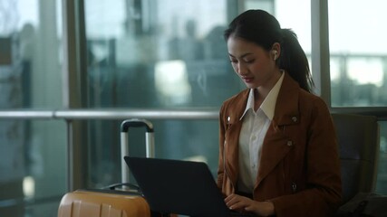 Confident young asian businesswoman working remotely online using laptop at the airport terminal while waiting for her flight, young female browsing the internet for emailing and managing e-business.
