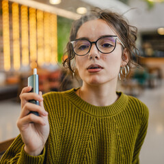 Young woman smoking electronic cigar while sit in cafe